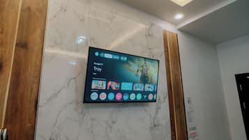 Een flatscreen televisie bevestigd aan een marmeren muur, met een Google TV interface en verschillende streaming apps.