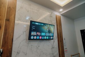 Un televisor de pantalla plana montado en una pared de mármol, mostrando una interfaz de Google TV con diversas aplicaciones de transmisión.