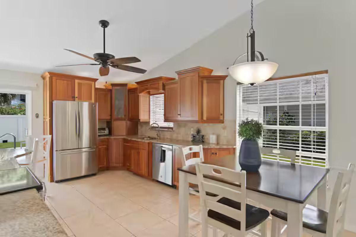 A kitchen with wooden cabinets, stainless steel appliances, a ceiling fan, and a dining area with a table and chairs.