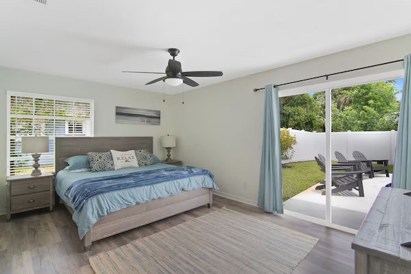Quarto com cama, ventilador de teto, janela com persianas e vista para o quintal através de uma porta de correr.