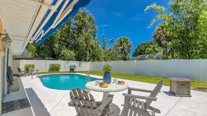 En baghave med swimmingpool, udendørs møbler og en overdækket terrasse.