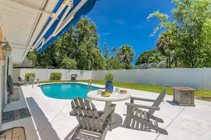 Um quintal com piscina, móveis de jardim e um espaço coberto de varanda.