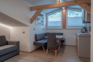 A compact kitchen with a dining area, wooden beams, and a window with blinds. - Apartment Haus Dienten - Top 9 (Dienten am Hochkönig)
