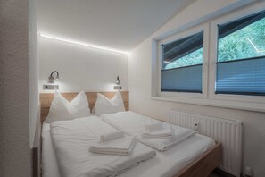 Ein Schlafzimmer mit einem Holz-Kopfteil, einem großen Fenster mit Jalousien, zwei Wandleuchten und einer Heizung.