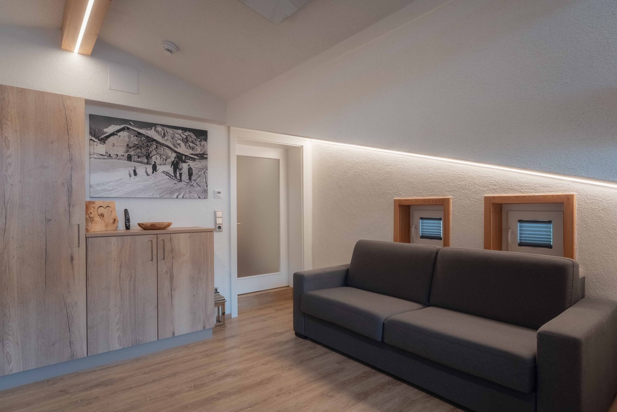 Ein modernes Interieur mit einem Holzkabinent, einem grauen Sofa und einem an der Wand befestigten Bild.