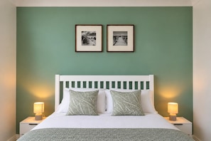A bed with a white headboard, two pillows with leaf patterns, and two bedside lamps.