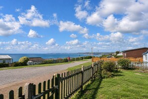 A coastal property with a gravel driveway, wooden fence, and a view of the sea. - Jesmondene (Freathy)