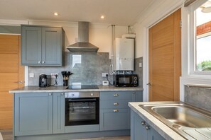 A modern kitchen with grey cabinets, a built-in oven, a microwave, and a water heater. - Jesmondene (Freathy)
