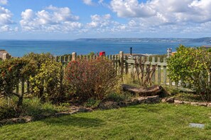 A coastal landscape with a wooden fence, grassy areas, and a view of the sea. - Jesmondene (Freathy)