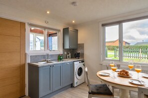 A compact kitchen with a washing machine, a sink, and a dining area with a table set for breakfast. - Jesmondene (Freathy)