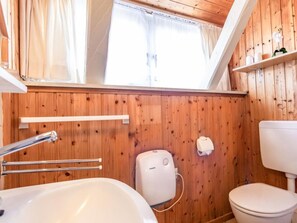A wooden-paneled bathroom with a white sink, toilet, and a window above the sink. - 3 in the House Sturmmowe (St. Peter-Ording)
