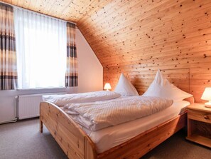 A bedroom with a sloped wooden ceiling, a bed with white bedding, a nightstand, and a window with curtains. - 3 in the House Sturmmowe (St. Peter-Ording)