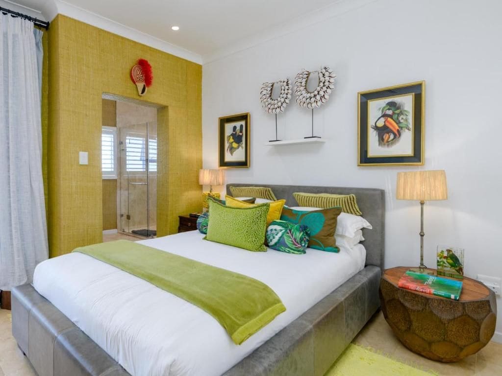 A hotel room with a large bed, a bedside table with a lamp, a small side table with books, and a shower area.