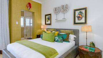 A hotel room with a large bed, a bedside table with a lamp, a small side table with books, and a shower area.