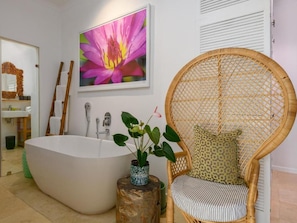 Casa de banho moderna com uma banheira independente, uma cadeira de vime com almofada e um grande quadro com flores na parede.