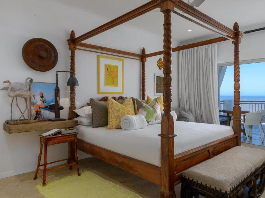 Una cama con dosel con vista al mar, una mesita de noche pequeña y un banco al pie de la cama.