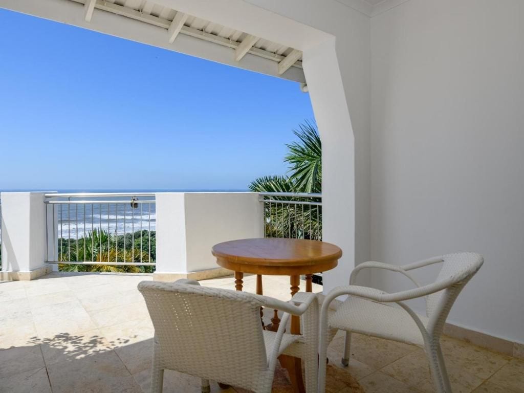 A balcony with a view of the sea, a round wooden table, and two wicker chairs.