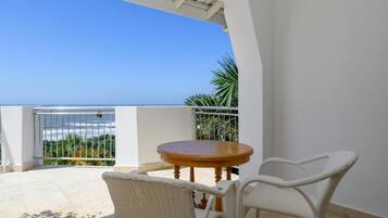 A balcony with a view of the sea, a round wooden table, and two wicker chairs.