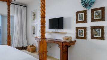 Ein Schlafzimmer mit einem Himmelbett, einem Fernseher auf einem Holzboden und gerahmten Bildern an der Wand.