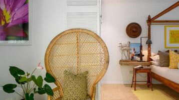 Quarto com cadeira de vime, sofá, planta em vaso e quadro na parede.