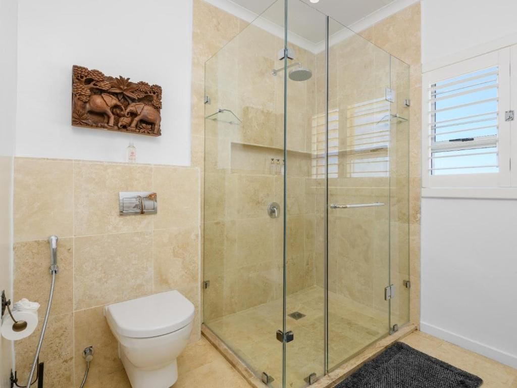 A bathroom with a glass shower enclosure, a toilet, and a decorative wall piece.
