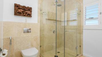 A bathroom with a glass shower enclosure, a toilet, and a decorative wall piece.