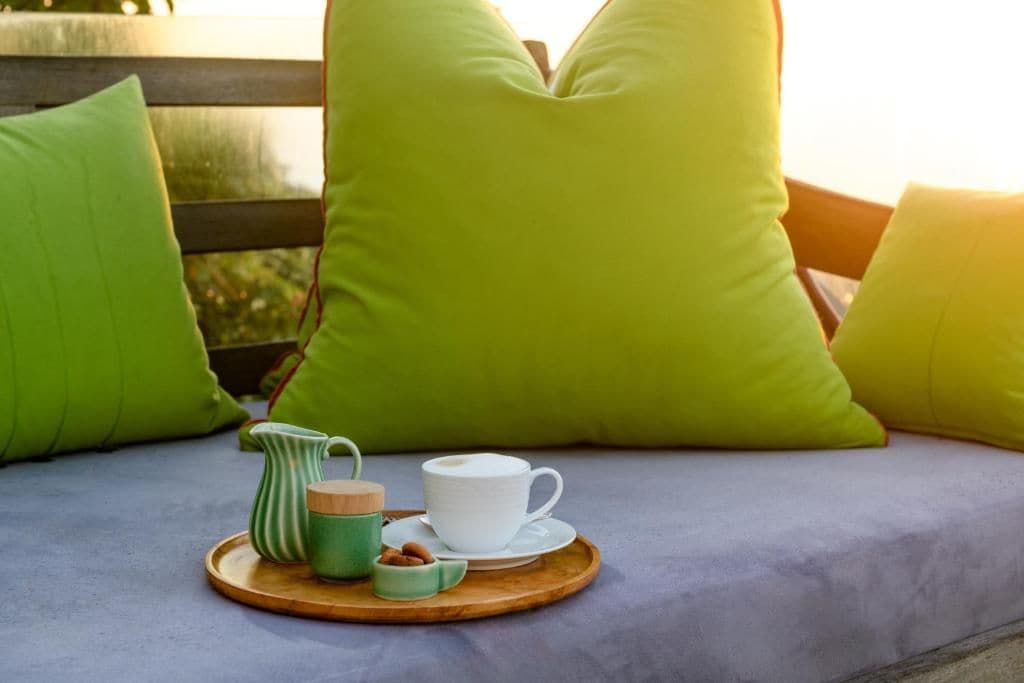 Un espace détente avec une table basse sur laquelle sont disposés une cafetière et des pâtisseries, des coussins verts et un banc en bois.