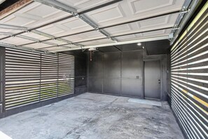 Eine Garage mit Betonboden, einer Metall-Garagentür und einer schwarzen Wand mit horizontalen Lamellen.