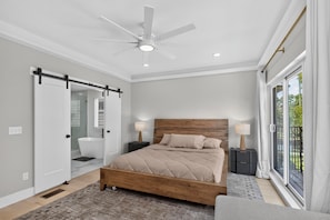 Ein Schlafzimmer mit Bett, Deckenventilator, Fenster mit Blick und einer Schiebetür.