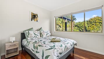 A bedroom with a bed, a nightstand, a lamp, a window with a view of trees, and a painting on the wall.