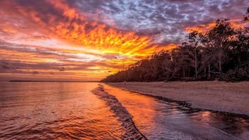 A sunset over a beach with a calm sea reflecting the sky.