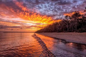 Ein Sonnenuntergang über einem Strand mit ruhiger See, die den Himmel spiegelt.