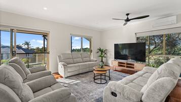 A spacious living room with a flat-screen TV, grey sofas, a coffee table, and a ceiling fan.