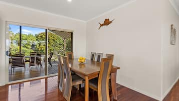 A dining area with a wooden table and chairs, a glass door leading to an outdoor patio with chairs and a table, and a wall-mounted decorative piece.