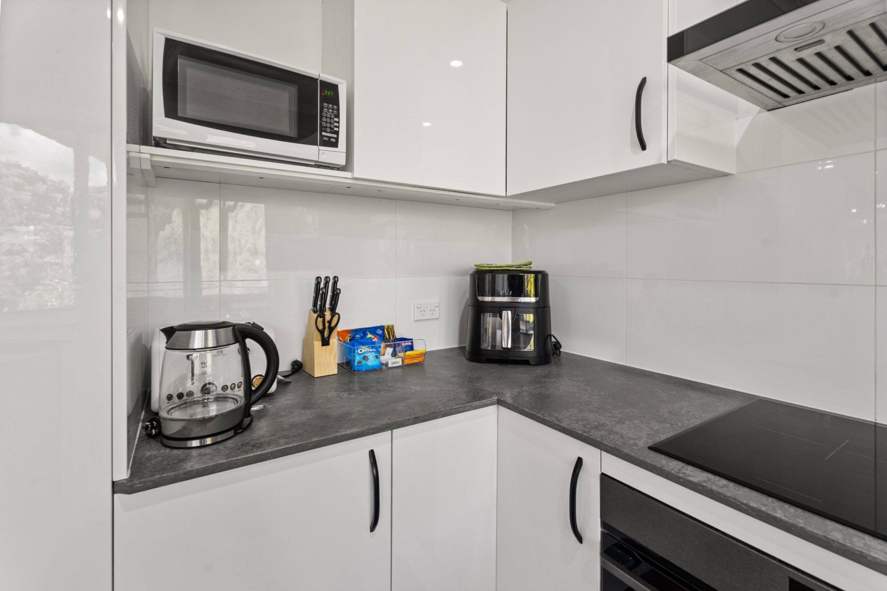 A modern kitchen with white cabinets, a microwave, a coffee maker, and a kettle.