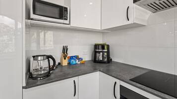A modern kitchen with white cabinets, a microwave, a coffee maker, and a kettle.