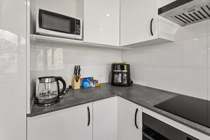 Eine moderne Küche mit weißen Schränken, einer Mikrowelle, einer Kaffeemaschine und einem Wasserkocher.
