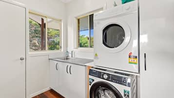 A compact laundry room with a front-loading washing machine, a sink, and a window with a view of greenery.