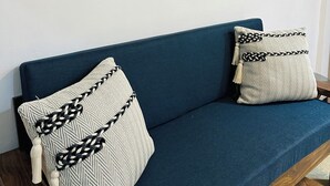 Een blauwe bank met gekleurde kussens tegen een witte muur, met een lijstwerk erboven.