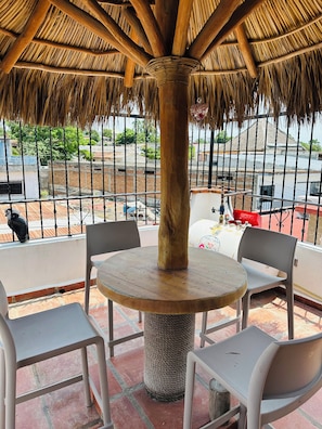 A thatched-roof outdoor seating area with a round table and chairs, overlooking a residential area. - Affordable 1 Bedroom with Amazing Rooftop Terrace - Great Bucerias Location (Bucerías)