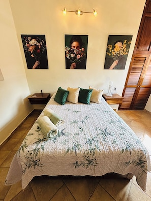 A hotel room with a bed, pillows, a nightstand, a lamp, and wall art. - Affordable 1 Bedroom with Amazing Rooftop Terrace - Great Bucerias Location (Bucerías)