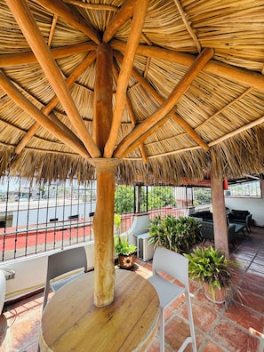 A covered outdoor seating area with a thatched roof, a round table, and potted plants. - Affordable 1 Bedroom with Amazing Rooftop Terrace - Great Bucerias Location (Bucerías)