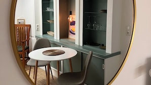Quarto com espelho redondo refletindo uma sala de jantar, cozinha com prateleira embutida e pequena mesa com cadeiras.