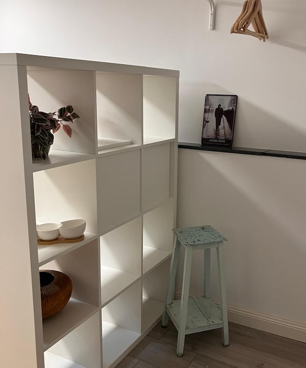 A white shelving unit with multiple compartments, a small stool, and a framed picture on the wall.