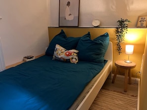 Una cama con ropa de cama color turquesa, una almohada estampada, una mesita de noche con una lámpara y un reloj de pared.