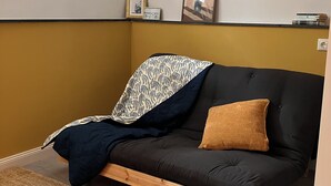 Um quarto com um sofá de cor escura, um cobertor estampado, uma almofada marrom e um tapete tecido.