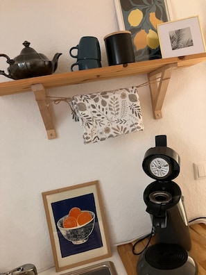 A kitchen with a coffee maker, a kettle, and a framed picture of oranges.