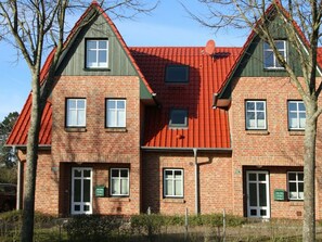 Ein zweistöckiges Backsteinhaus mit rotem Ziegeldach, mehreren Fenstern und einer Tür.