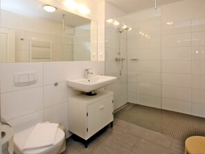Ein modernes Badezimmer mit einem weißen Waschbecken, einem Spiegel und einer Dusche.