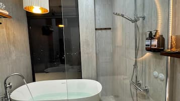 Et stilfuldt badeværelse med et fristående badekar, en glasafskærmet brusekabine og et håndvaskarrangement med toiletartikler.